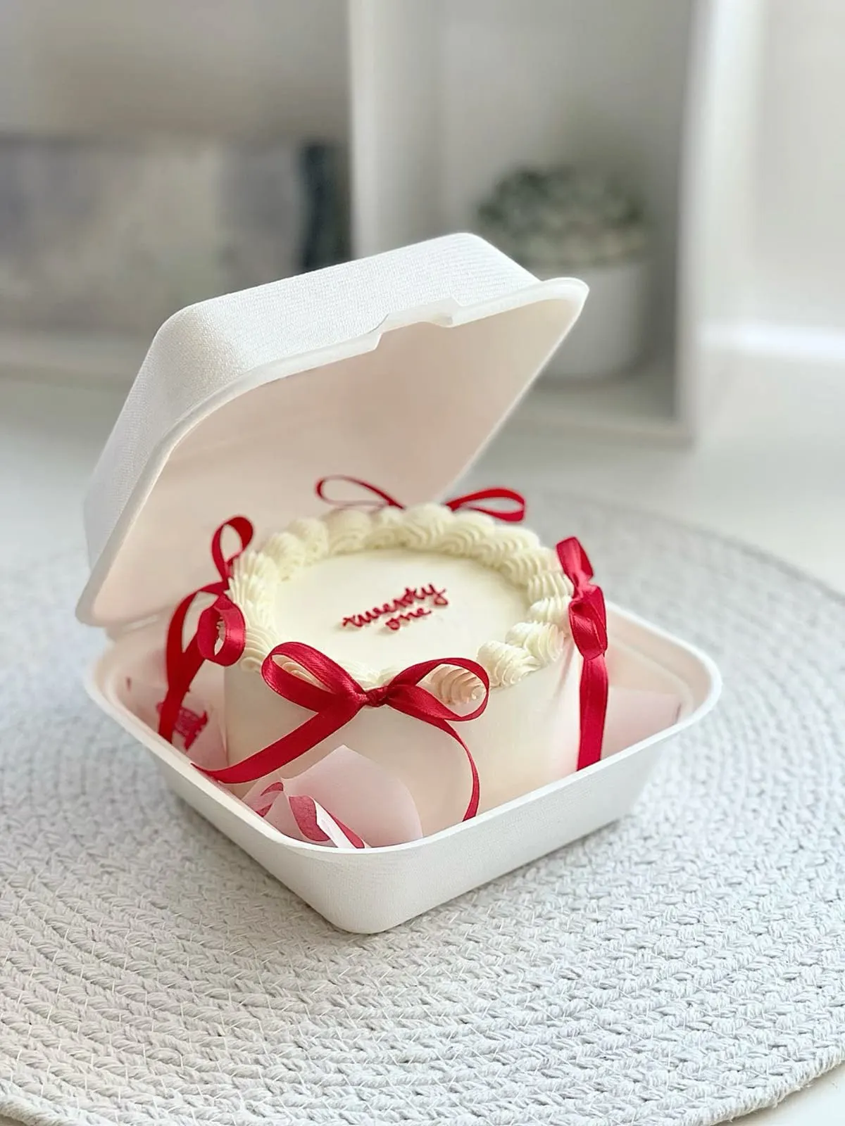 Witte bento cake versierd met spuitwerk en rode linten, gemaakt tijdens de bento cake workshop