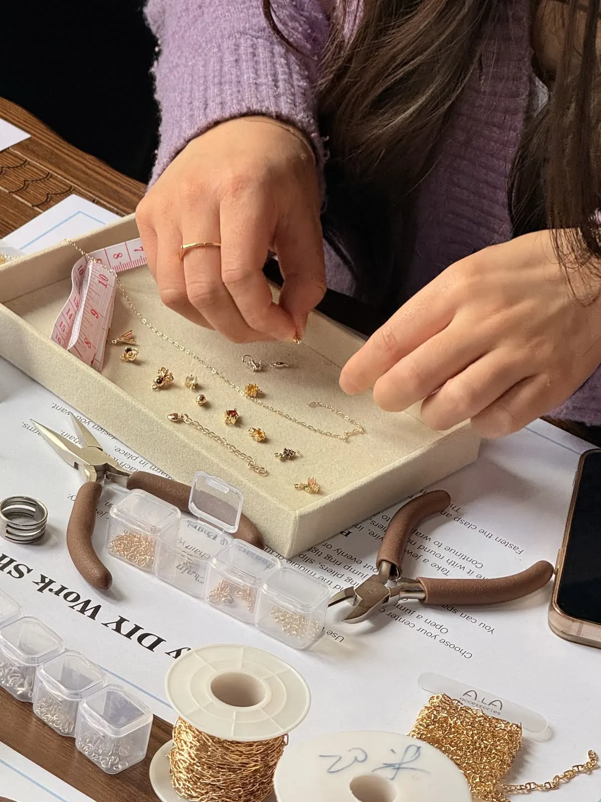 Handen die gouden bedels kiezen om een ketting samen te stellen tijdens de juwelen workshop