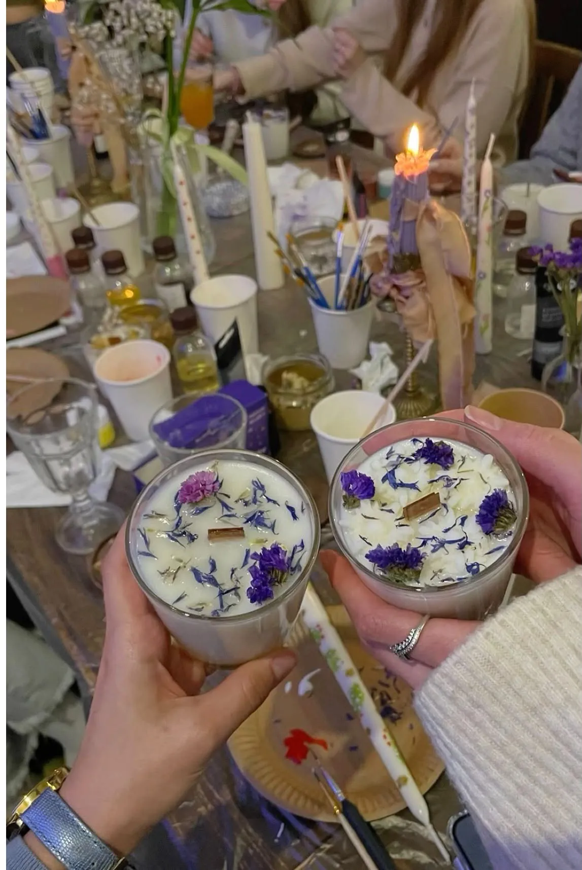 Twee deelnemers houden hun met droogbloemen versierde kaarsen vast na de kaarsen workshop